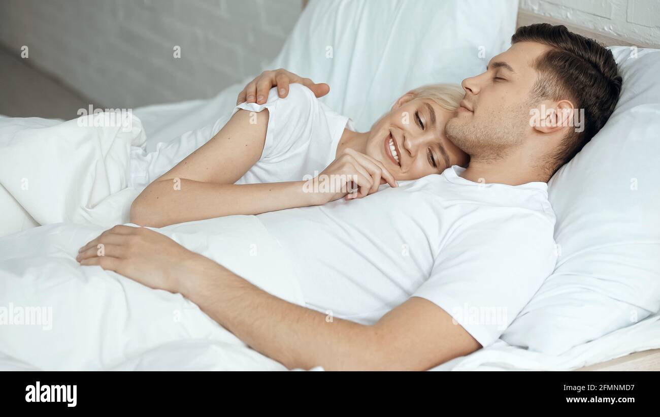 Glückliche blonde Frau, die sich im Bett mit ihrem Freund ausruhte Stockfoto