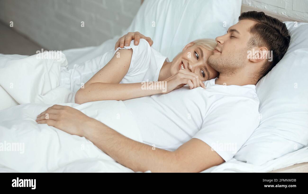 Fröhliche blonde Frau, die sich im Bett mit ihrem Freund ausruhte Stockfoto