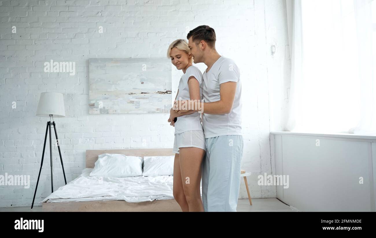 Glücklicher Mann umarmt junge blonde Frau im Schlafzimmer Stockfoto