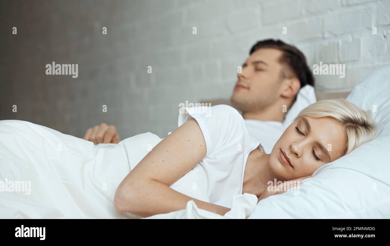 Blonde Frau schläft im Bett mit Mann in verschwommenem Hintergrund Stockfoto