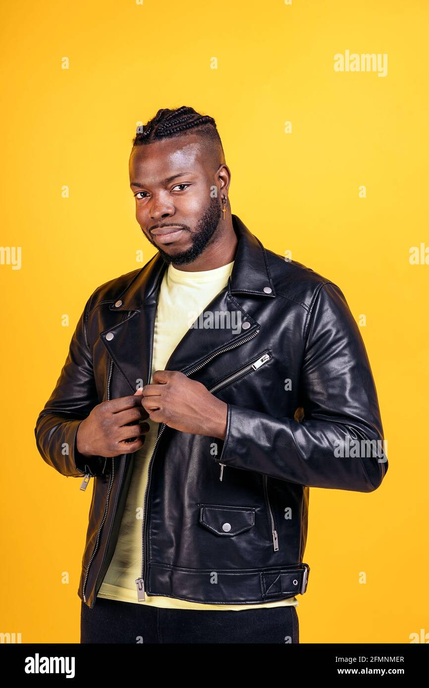 Starker schwarzer Mann mit schwarzer Lederjacke posiert im Studio vor gelbem Hintergrund. Stockfoto