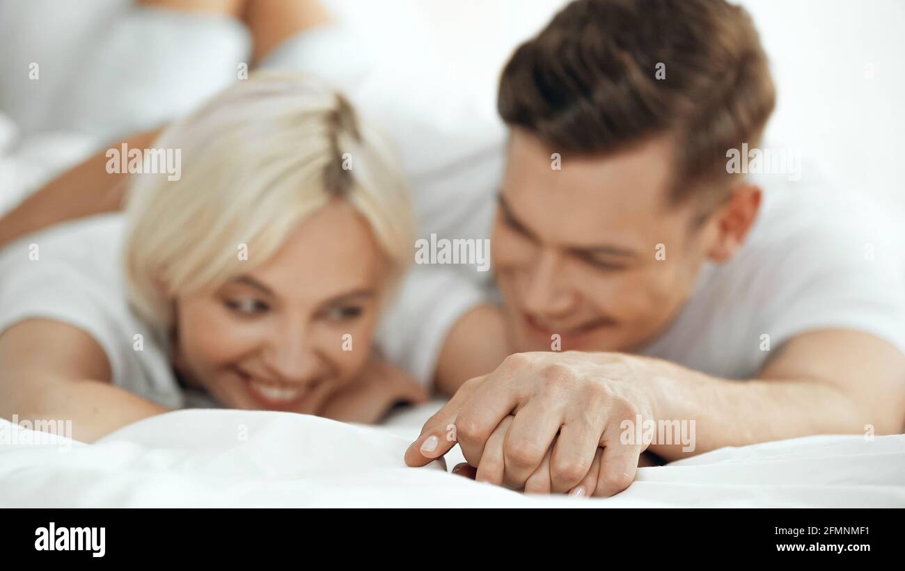 Verschwommener junger Mann und Frau, die die Hände hielten und lächelten Bett Stockfoto