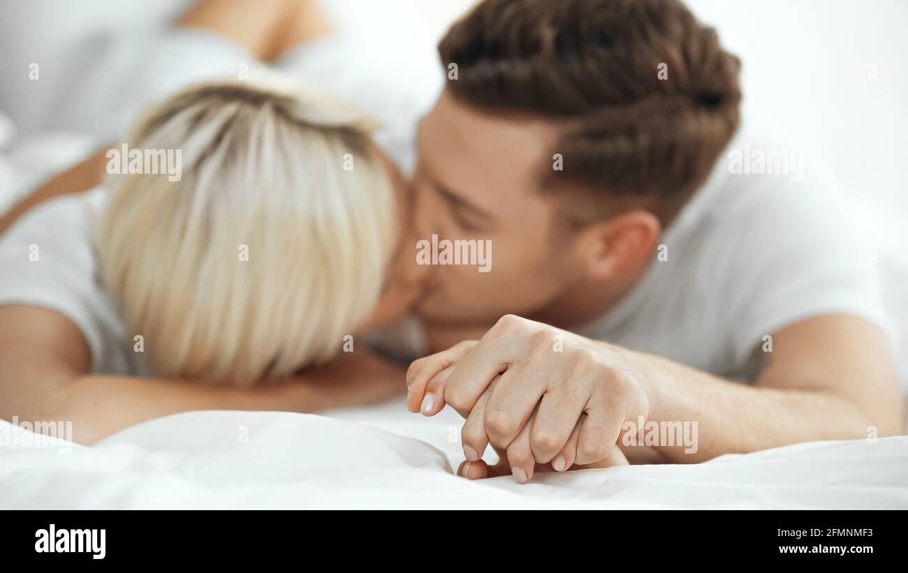 Verschwommene junge Frau und Mann, die Hände hielten und sich küssten Bett Stockfoto