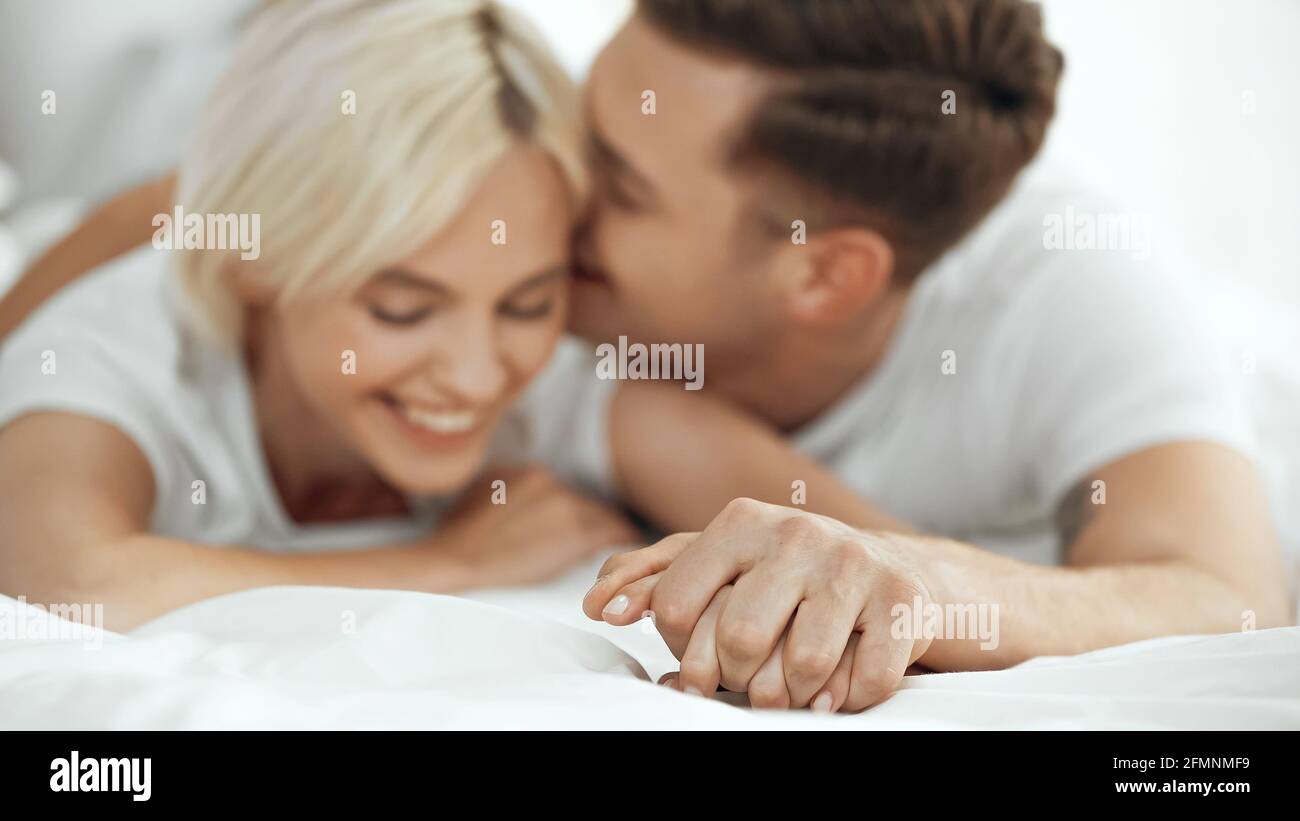 Verschwommene junge Frau und Mann, die Hände hielten und lächelten Bett Stockfoto