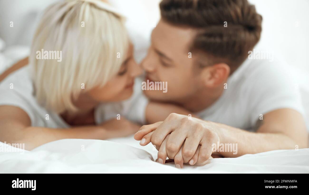 Verschwommene Frauen und Männer halten die Hände und lächeln im Bett Stockfoto