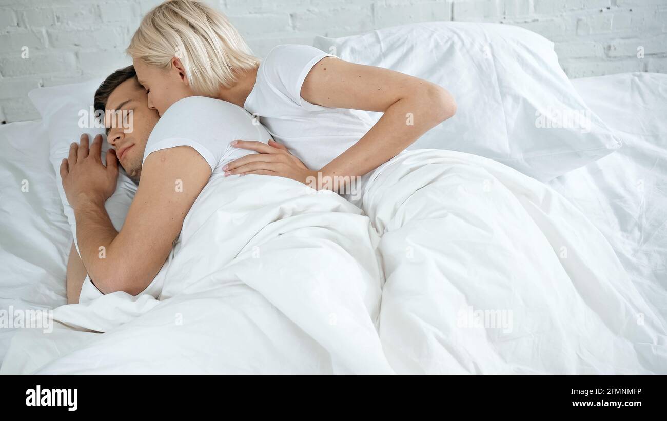 Junge Frau küsst jungen Mann schlafen im Bett Stockfoto