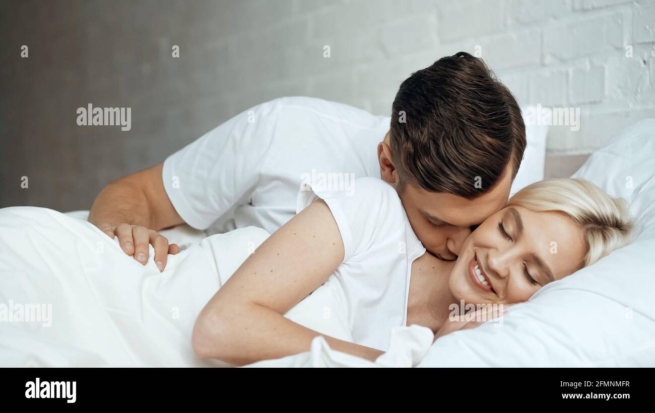 Glücklicher Mann küsst lächelnde Frau liegend mit geschlossenen Augen Bett Stockfoto