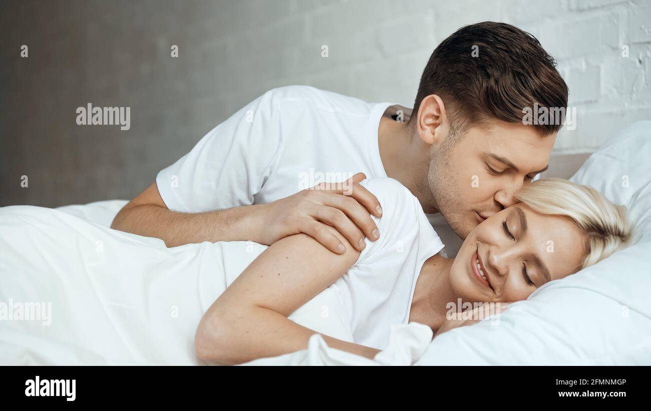 Glücklicher Mann, der blonde Frau küsst und mit geschlossenen Augen liegt Bett Stockfoto