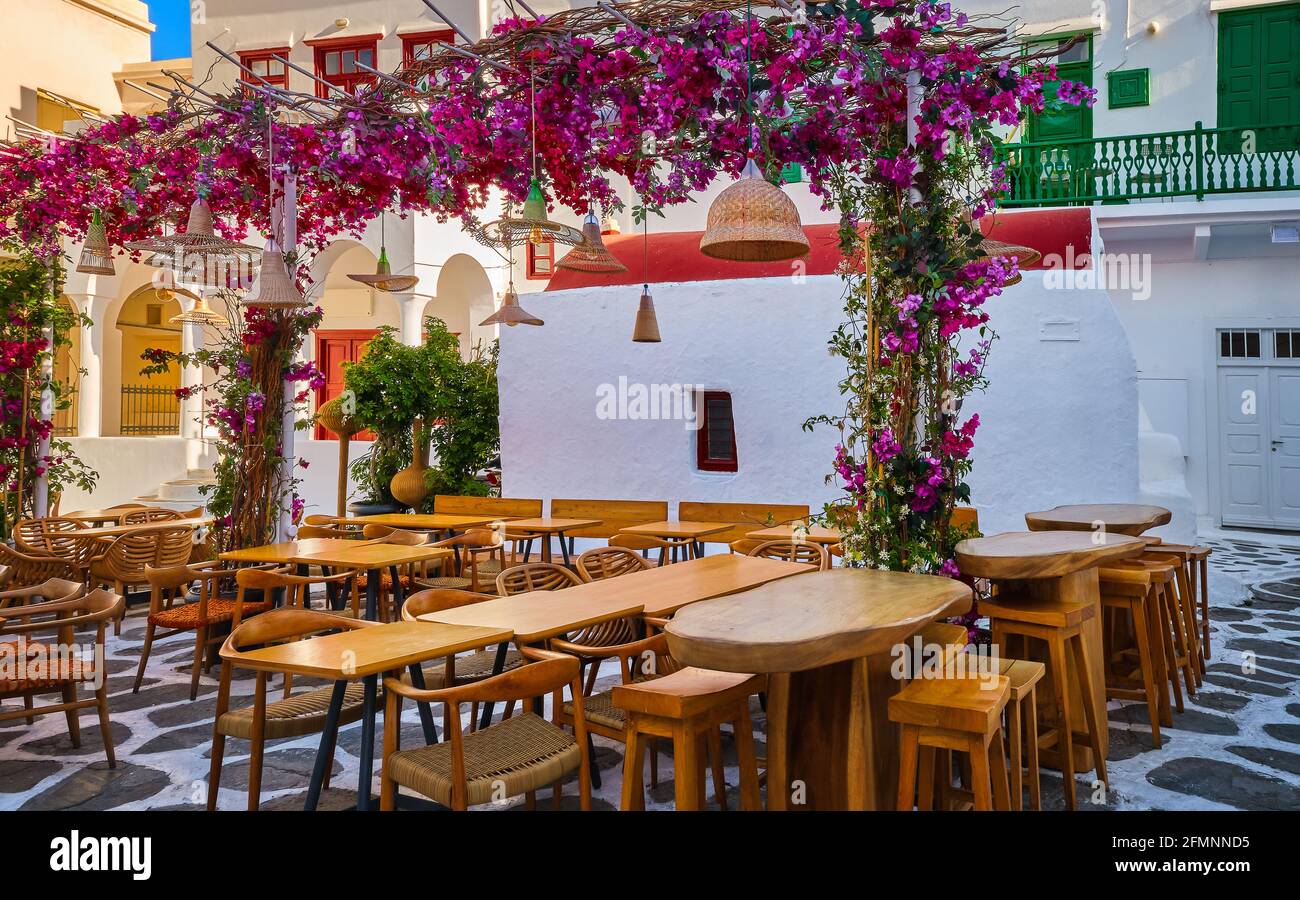 Gemütliches Essen im Freien, Café, Restaurant, Taverne auf dem kleinen griechischen Platz, weiß getünchte Kapelle, lebendige rosa Bougainvillea in voller Blüte. Mykonos, Griechenland Stockfoto