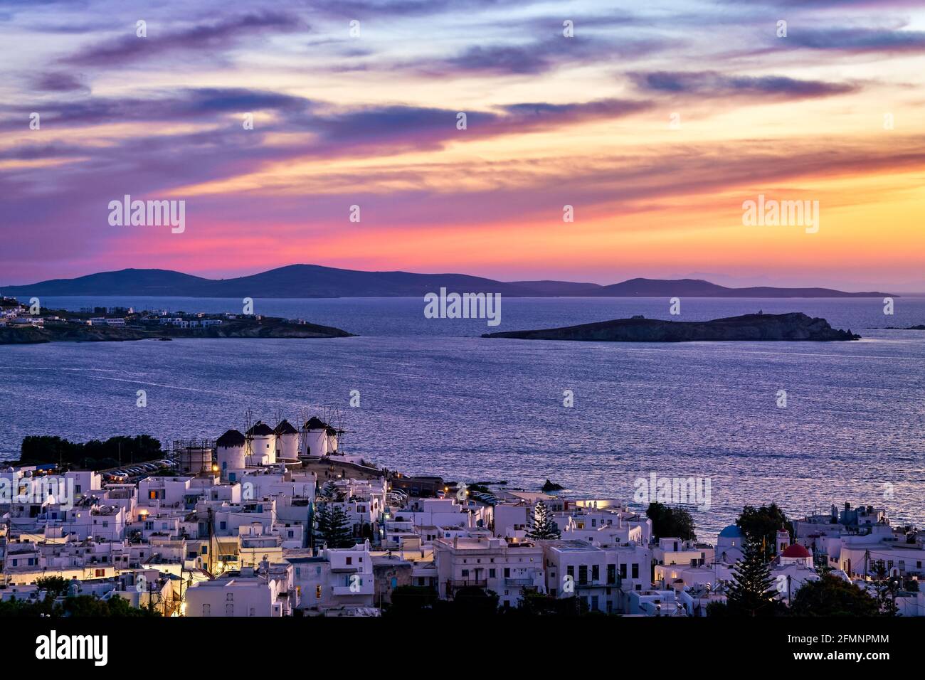 Farbenfrohe Sonnenuntergänge berühmte traditionelle weiße Windmühlen, Mykonos, Griechenland. Weiß getünchte Häuser, farbenprächtiger Sonnenuntergang, Sommerziel, Lichter der Stadt an Stockfoto