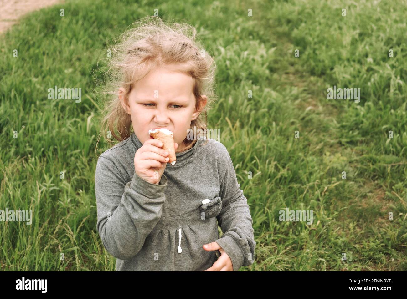 Porträt eines Kindes in der Natur. Speicherplatz kopieren. Schöne blonde Mädchen 4 Jahre alt. Grünes Gras Hintergrund. Das Kind isst kaltes Eis. Stockfoto