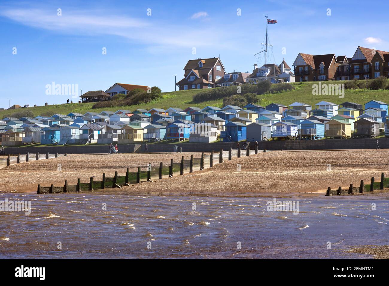 Reihen von bunten Strandhütten unter dem grasbewachsenen Hang bei Tankerton Beach, Whitstable, Kent, England, Großbritannien Stockfoto