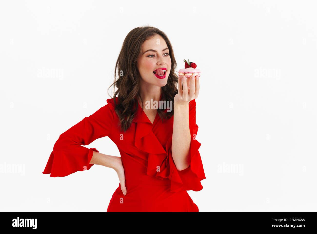 Schöne schöne junge Frau in rotem Kleid versucht zu essen Ein leckerer Kuchen auf weißem Hintergrund Stockfoto