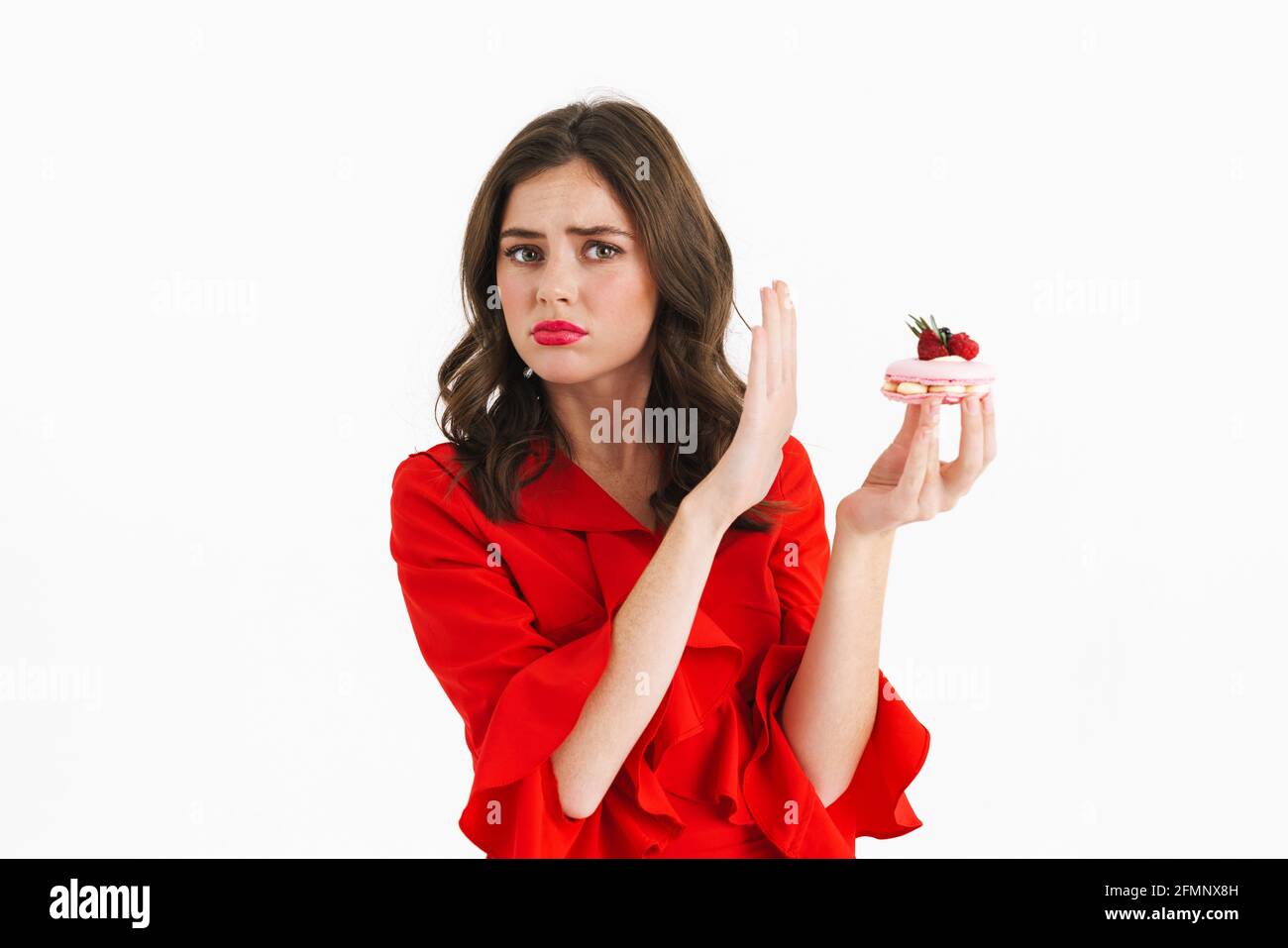 Schöne junge Frau in rotem Kleid weigert sich zu essen Ein leckerer Kuchen auf weißem Hintergrund Stockfoto