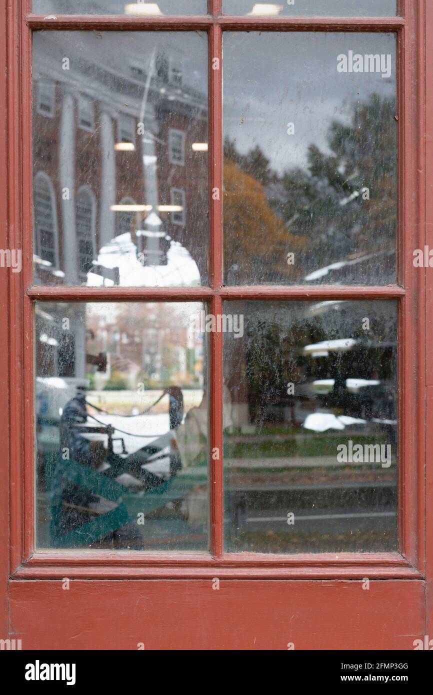 Ein Fenster im Weld Boat House in Cambridge, MA, mit Booten im Inneren und dem Blick dahinter und Reflektionen eines Gebäudes und Bäumen hinter dem Fotografen Stockfoto