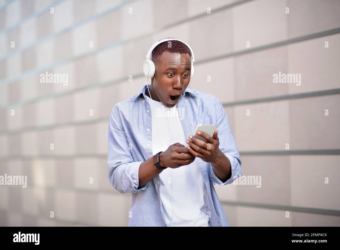 Schockierter afroamerikanischer Mann im Headset starrte auf den Smartphone-Bildschirm An der City Street Stockfoto