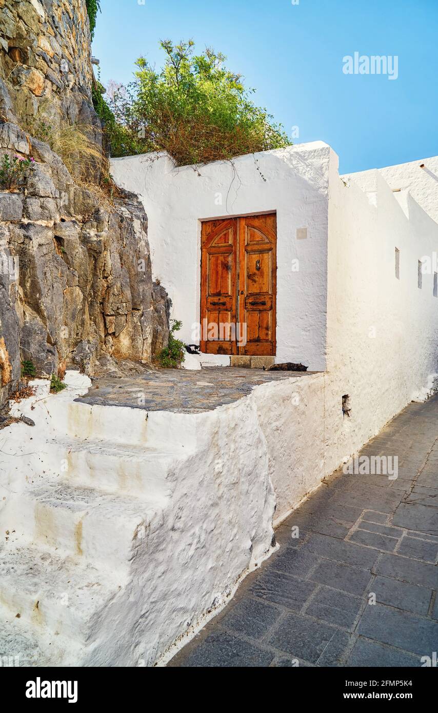 Enge, steile Straßen mit weiß getünchten Häusern und blühenden Büschen Und alte Treppen in der historischen griechischen Stadt Lindos unter Blau Himmel Stockfoto