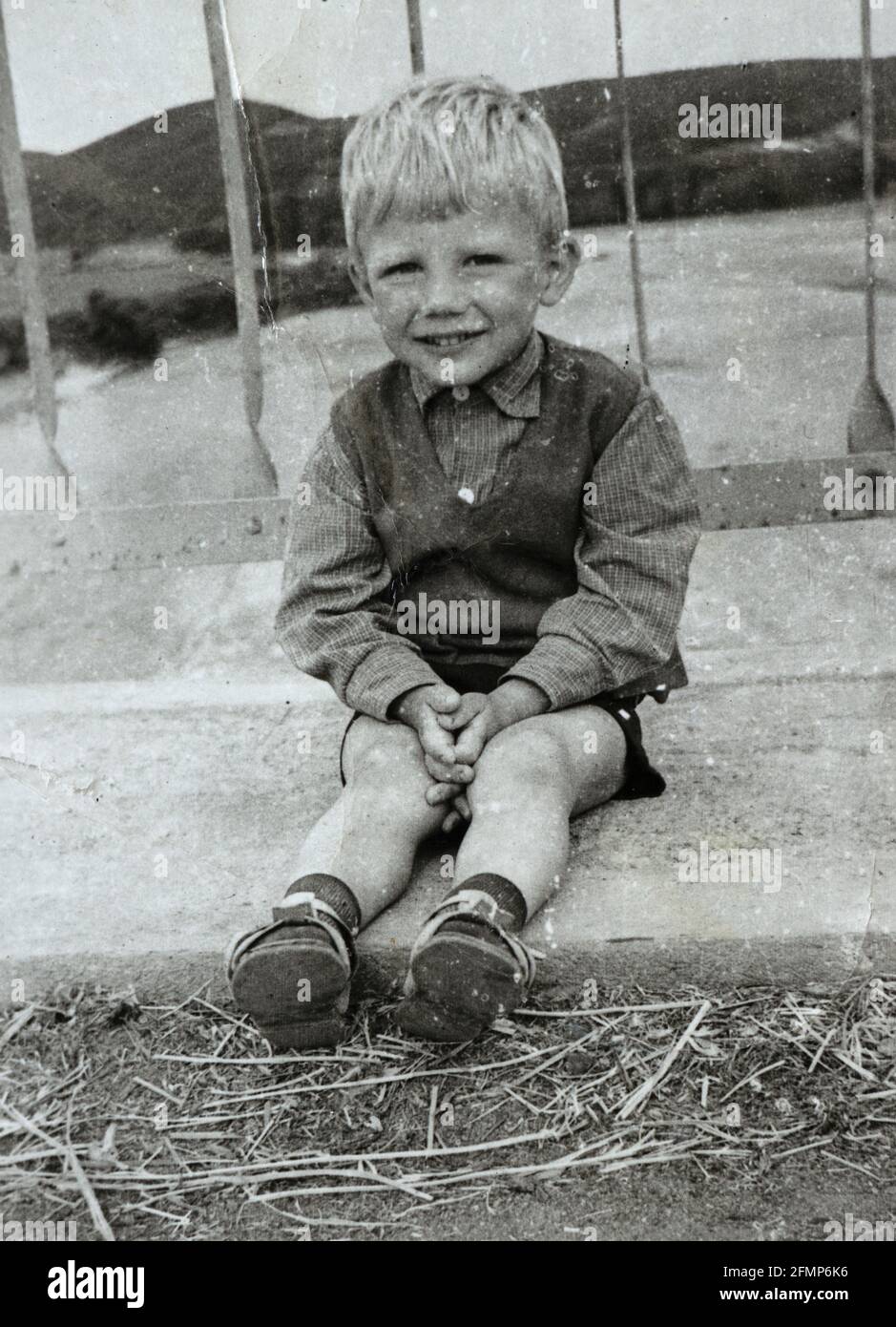 Lächelnder 4-jähriger Junge, der im Dreck auf einer Brücke um 1970, Bulgarien, sitzt Stockfoto