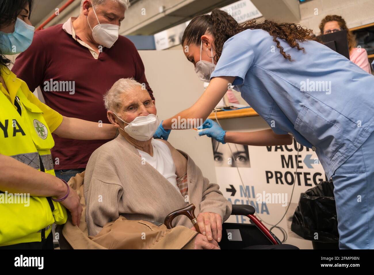 SAN Sebastián, SPANIEN – 08. Mai 2021: Ein älterer Mann im Rollstuhl erhält die Injektion der Dosis von einer jungen Krankenschwester im Impfzentrum CO Stockfoto