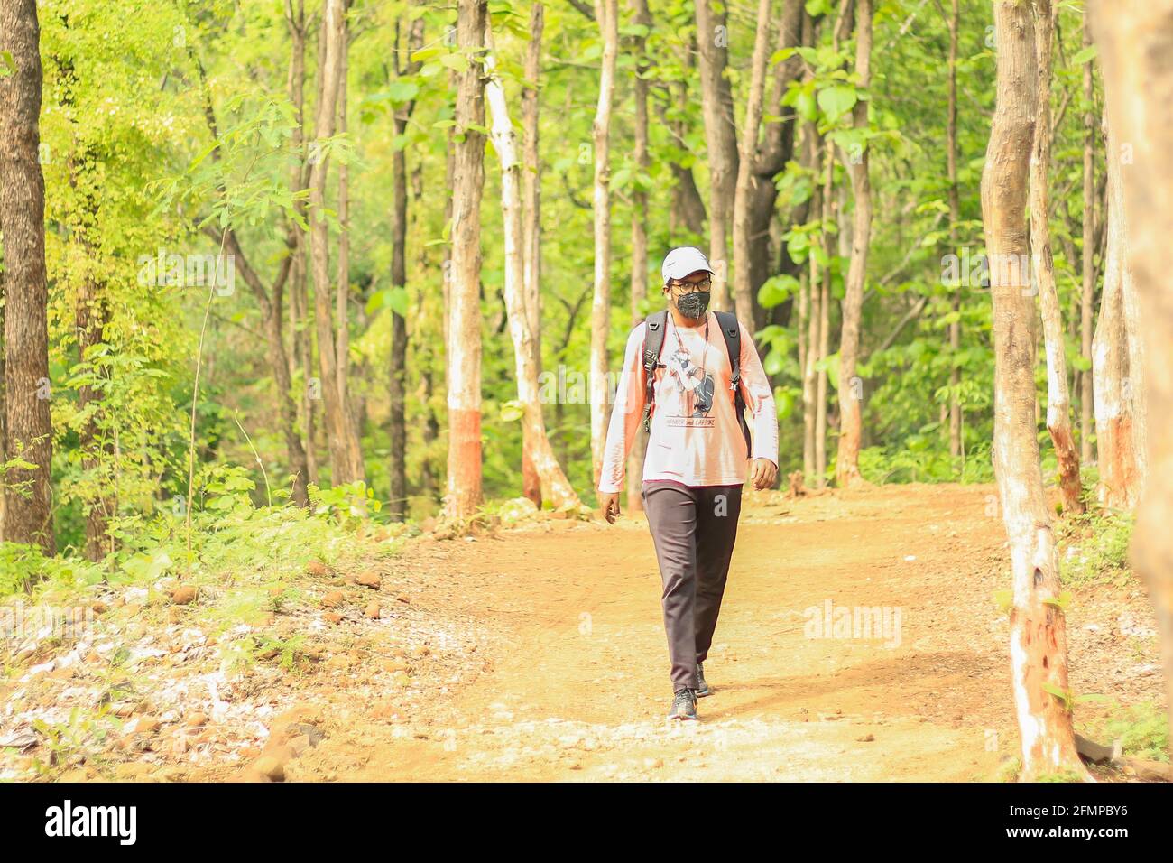 Ein 18-25-jähriger junger Inder mit Mütze und Maske inmitten einer Covid-19-Pandemie und frei und unabhängig in einem Dschungel zu Fuß. Stockfoto