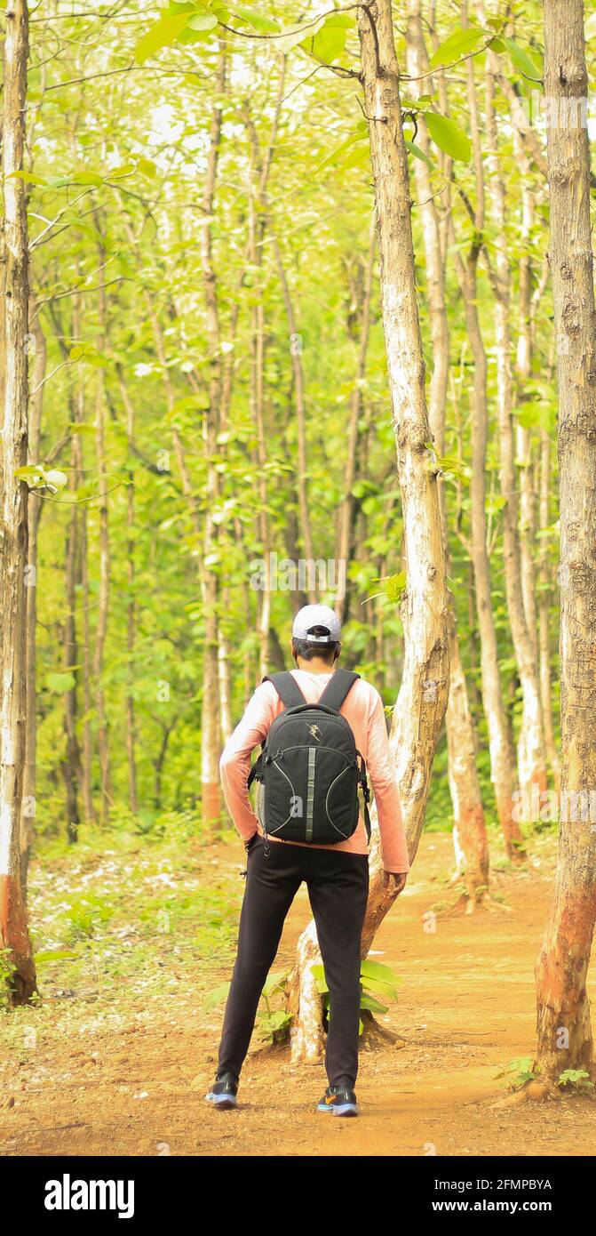 Ein 18-25-jähriger Mann, der eine Mütze trägt und mit einer Tasche in einem Wald steht. Volle Rückansicht eines indischen Mannes. Stockfoto