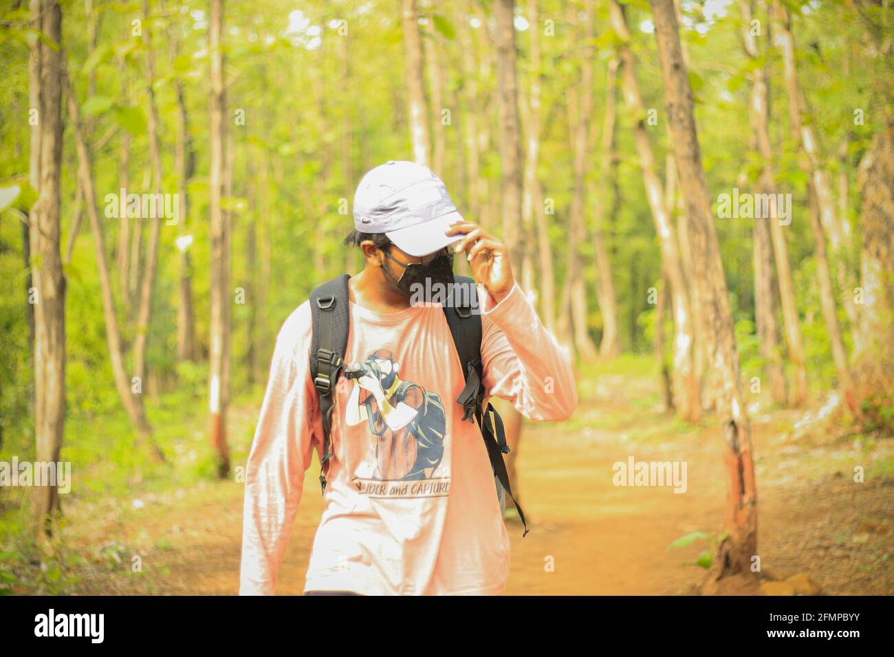 Ein 18-25-jähriger indischer Mann, der seine Mütze anpasst und eine Maske trägt und frei in einem Dschungel läuft. Zeigen Sie zur linken Seite der Kamera. Stockfoto