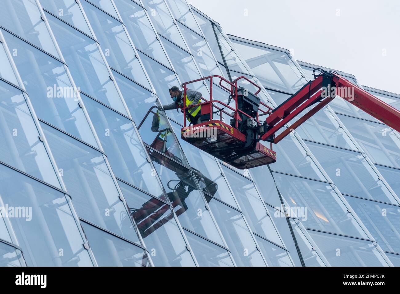 Kran mit Arbeiter an der Glasfassade mit Spiegelung Stockfoto
