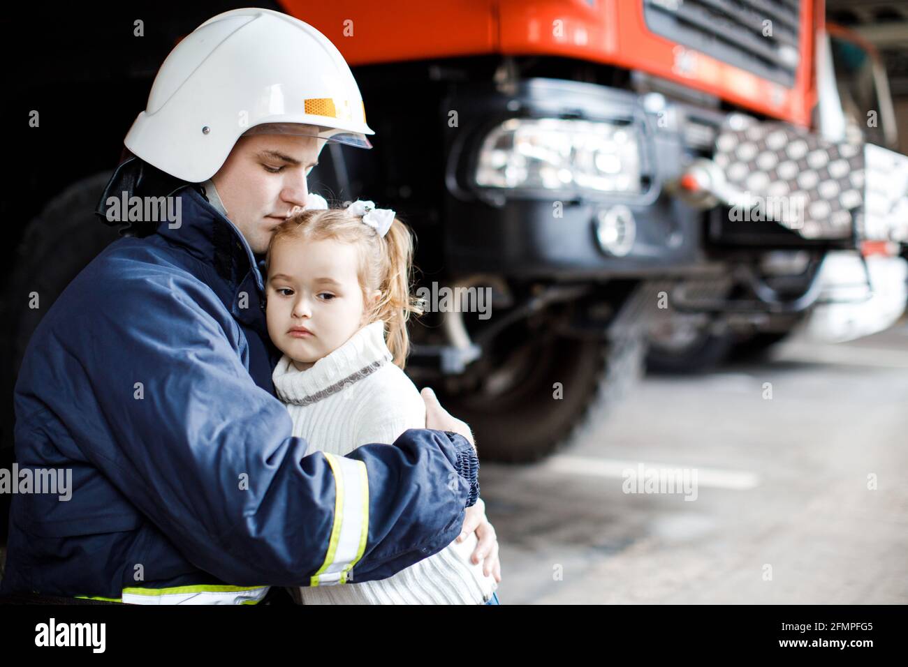 Tapferer Feuerwehrmann in Uniform hält kleines gerettete Mädchen aufrecht Schwarzer Hintergrund Stockfoto