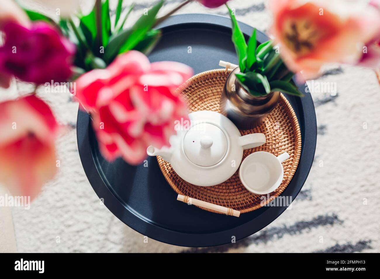 Inneneinrichtung und Inneneinrichtung. Frische Tulpen Blumen in Vasen auf Couchtisch mit Teekocher und Tasse auf Rattan Tablett. Draufsicht Stockfoto