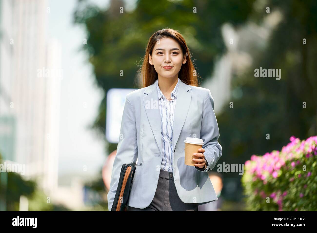 Erfolgreiche junge asiatische weibliche Führungskraft, die auf der Straße hält Eine Tasse Kaffee beim Betrachen der Kamera Stockfoto