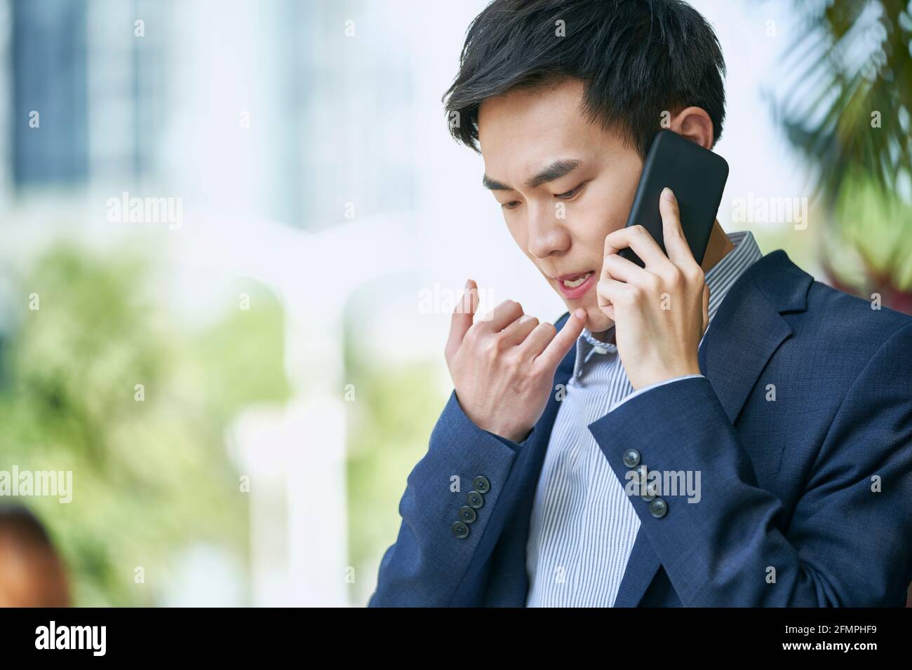 Junger asiatischer Geschäftsmann, der im Freien mit dem Handy spricht Stockfoto