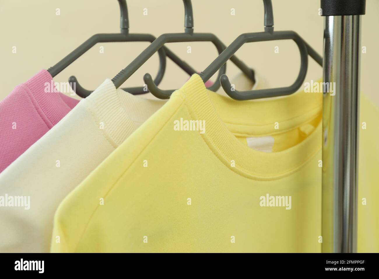 Kleiderständer mit Sweatshirts auf beigefarbenem Hintergrund Stockfoto