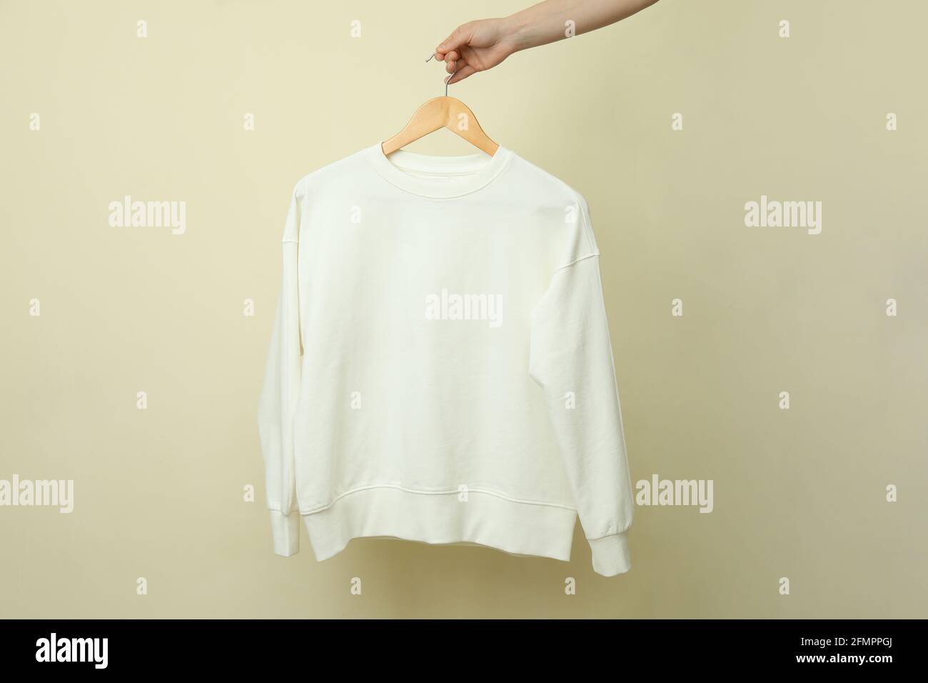 Kleiderbügel mit weißem Sweatshirt auf beigem Hintergrund Stockfoto