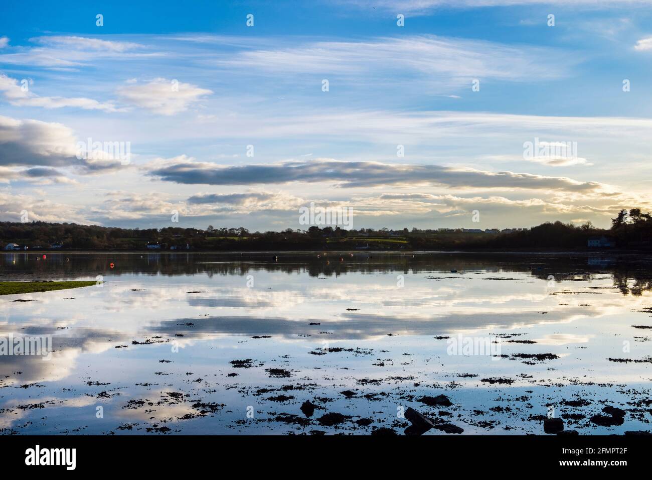 Ruhige Szenerie mit weißen Wolken und Himmel, die sich bei Flut in der Wintersonne im ruhigen Meer widerspiegeln. Red Wharf Bay, Isle of Anglesey, Wales, Großbritannien Stockfoto