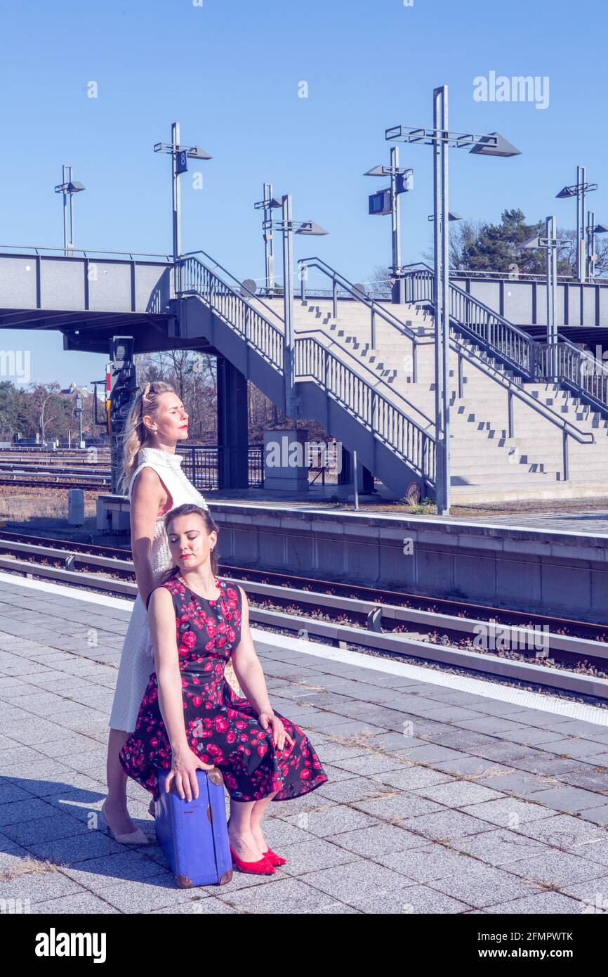 Zwei schöne Frauen im Stil der 1950er Jahre am Bahnhof warten Und die Sonne genießen Stockfoto