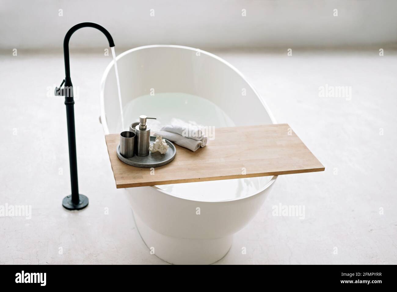 Die weiße Badewanne füllt sich mit Schaumwasser in einem modernen Apartment mit stilvoller Einrichtung im Loft-Stil und Wohneinrichtung. Spa-Konzept, Entspannung. Weich selektiv Stockfoto