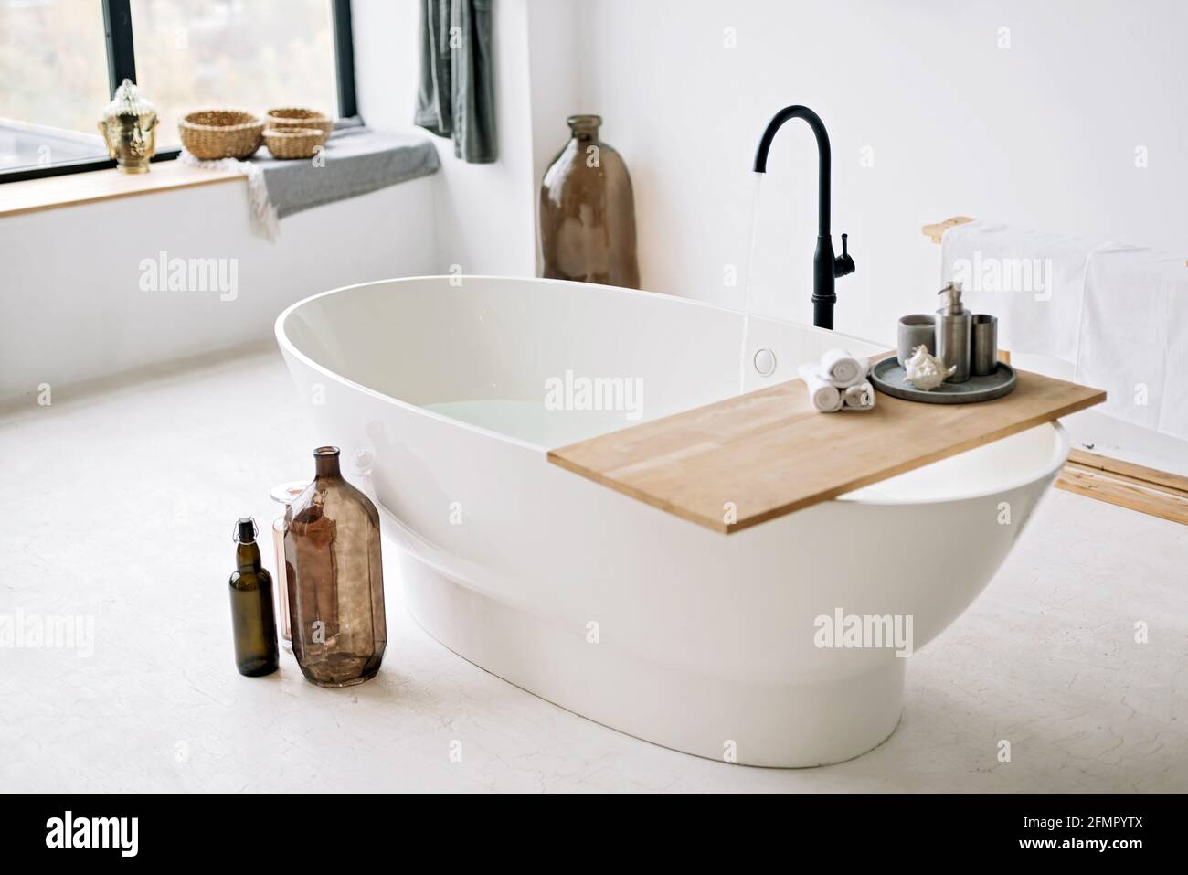 Die weiße Badewanne füllt sich mit Schaumwasser in einem modernen Apartment mit stilvoller Einrichtung im Loft-Stil und Wohneinrichtung. Spa-Konzept, Entspannung. Weich selektiv Stockfoto