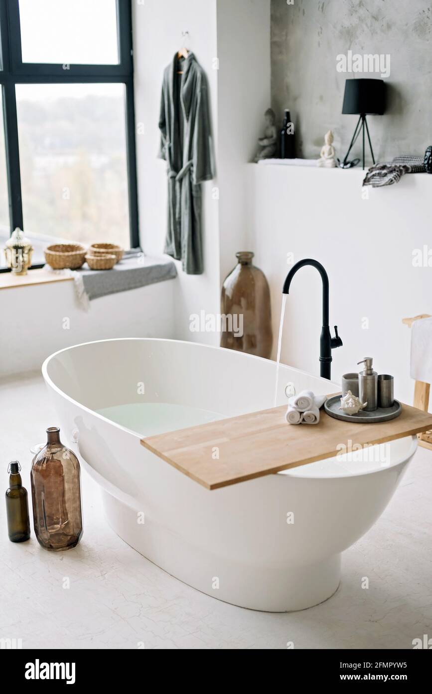 Die weiße Badewanne füllt sich mit Schaumwasser in einem modernen Apartment mit stilvoller Einrichtung im Loft-Stil und Wohneinrichtung. Spa-Konzept, Entspannung. Weich selektiv Stockfoto