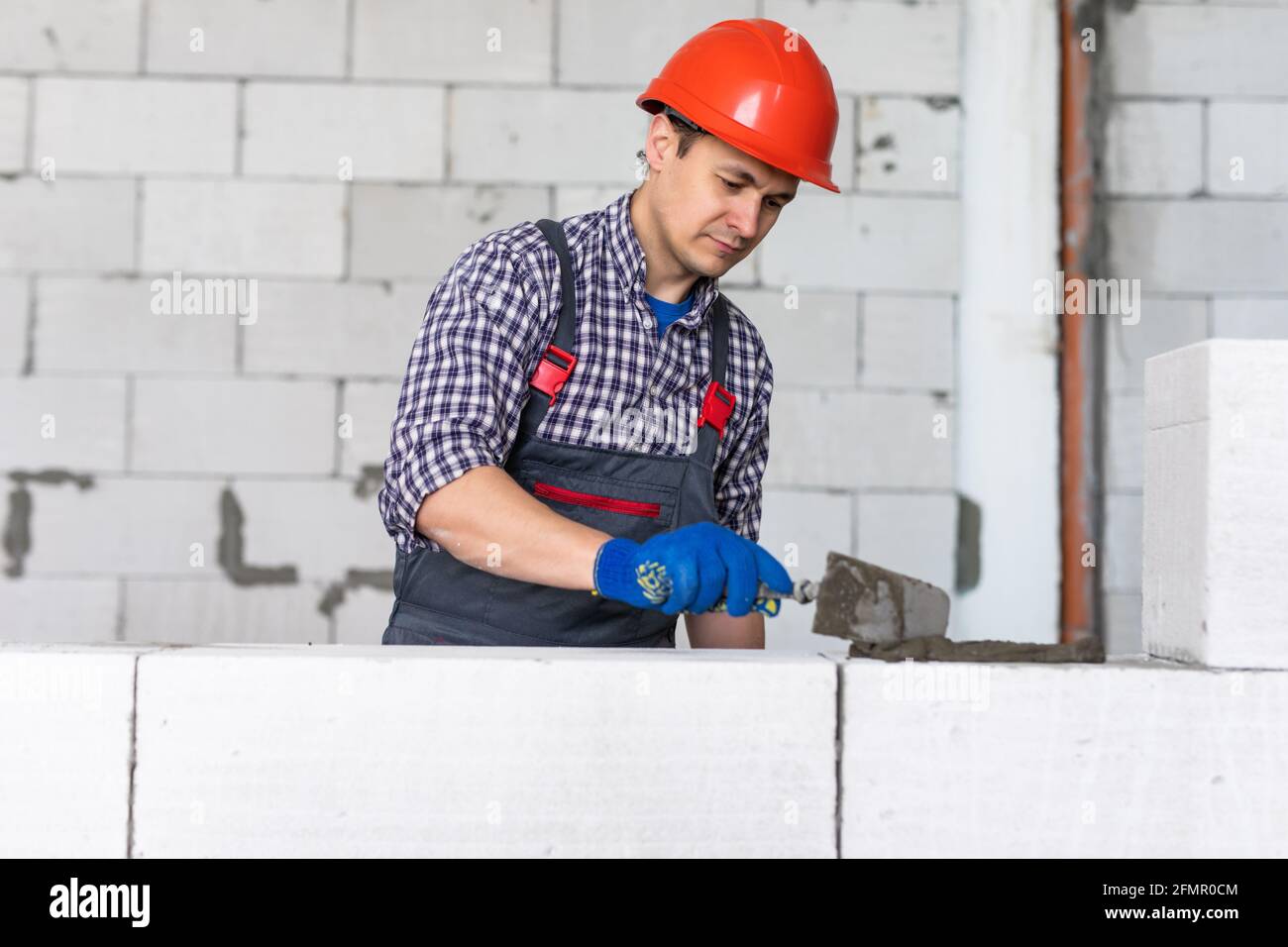 Der junge Baumeister legt einen Porenbetonblock an Stockfoto