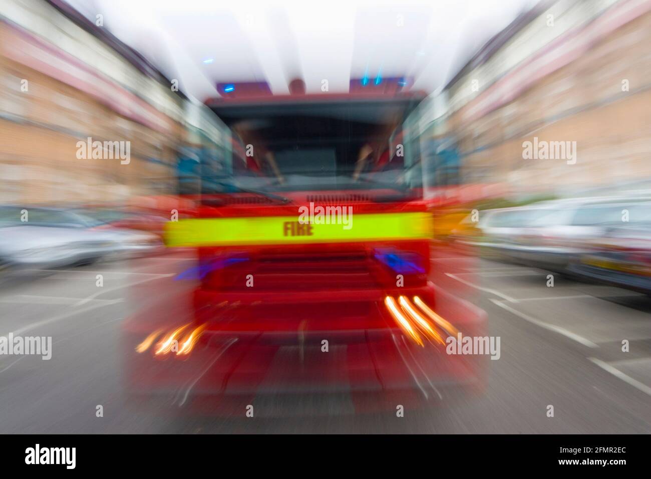 Bewegung verschwommenes Feuerwehrfahrzeug mit Feuerwehrauto, das sich bewegt Geschwindigkeit auf einer Straße durch Autos Verkehr und Gebäude Stockfoto