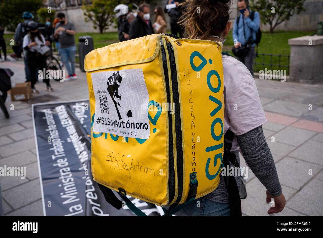 Ein Glovo-Händler vor der Puerta de Moncloa, der während der Demonstration ein Banner vorbereitet.Dutzende von "Reitern" (Lebensmittelhändler) demonstrieren und behaupten, ihre Arbeit als Freiberufler und gegen die Bedingungen von Lieferfirmen wie Globo und Deliveroo zu leisten. Heute Morgen verabschiedete Spanien das "Riders Law" und gab Unternehmen eine Frist von 3 Monaten, um Leute einzustellen, anstatt sie als falsche Freiberufler zu haben. Die Ministerin für Arbeit und Sozialwirtschaft, Yolanda Díaz, wies darauf hin, dass Spanien das erste Land sein wird, das einen Standard für digitale Plattformen hat. Stockfoto