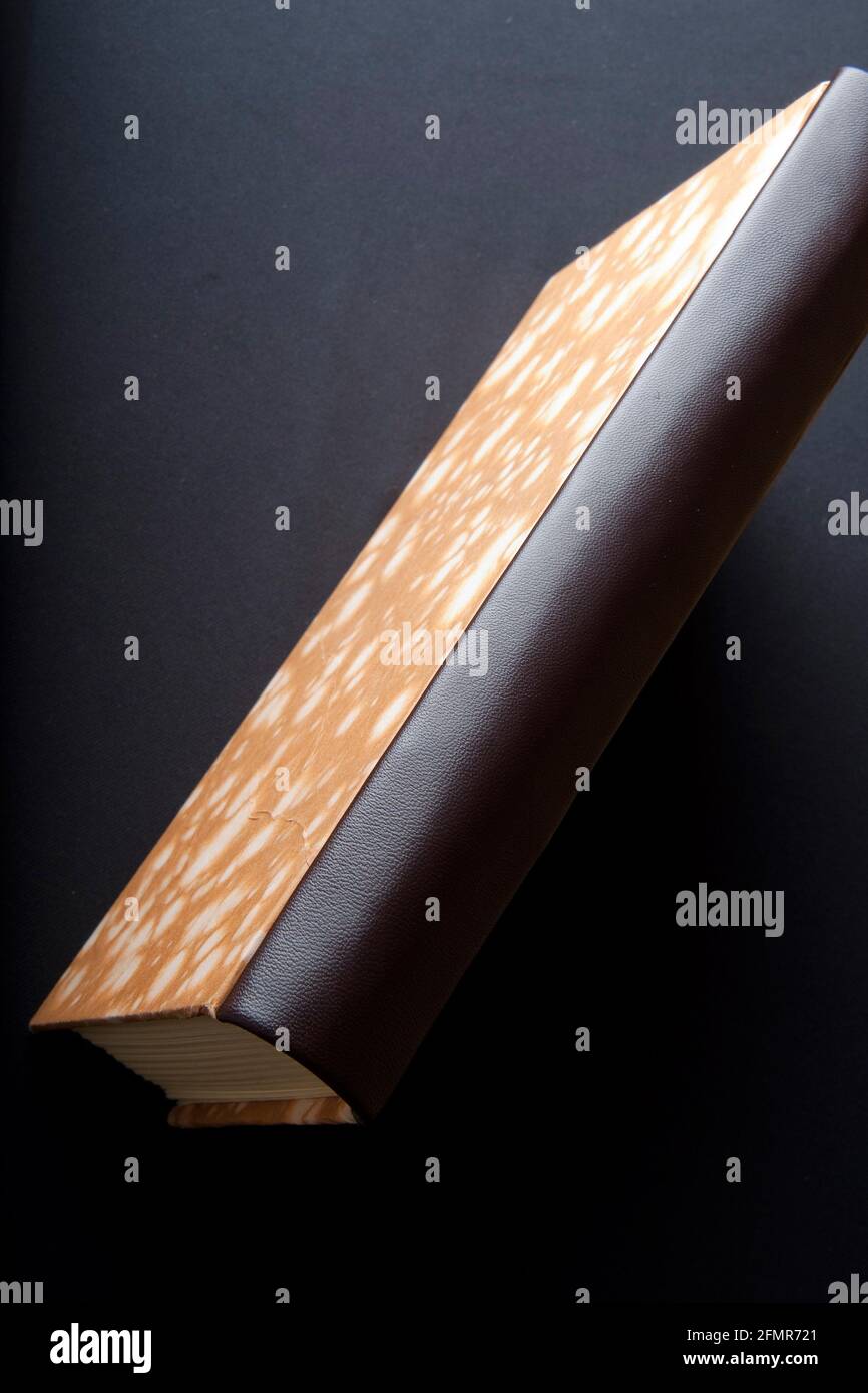 Art of Book Binding; handgefertigtes Buch mit Marmorpapierfront und Lederrücken. Nahaufnahme des Lederrückens. Schwarzer Hintergrund Stockfoto
