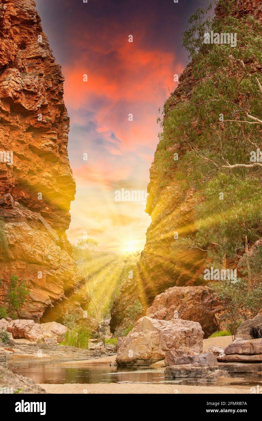 Sonnenaufgang in der Simpsons Gap Gorge in den West MacDonnell Ranges Im Northern Territory von Australien mit roten steilen Felsen und Sonne mit hellen Sonnenstrahlen Stockfoto