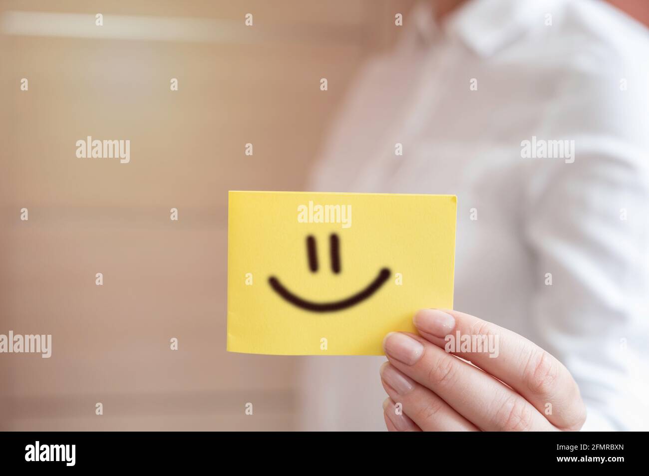 Die Hand des Kunden zeigt ein Feedback mit einer gelben Smiley-Gesichtskarte. Servicebewertung, Zufriedenheitskonzept Stockfoto