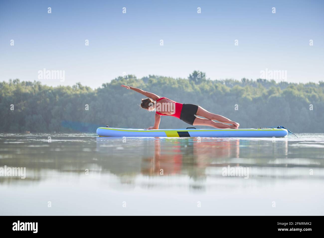 Frau meditiert und praktiziert Yoga während des Sonnenaufgangs im Paddle Board Stockfoto