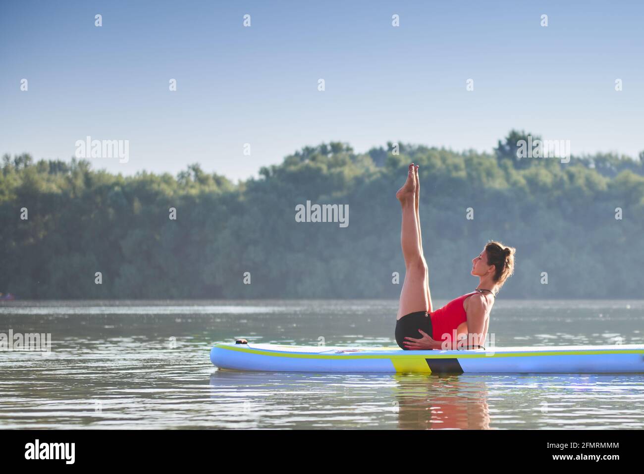 Frau meditiert und praktiziert Yoga während des Sonnenaufgangs im Paddle Board Stockfoto