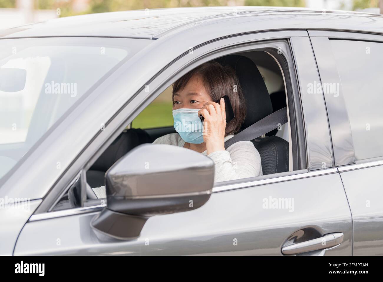 Reife asiatische Frau in einem Auto, die am Telefon spricht: Selektiver Fokus. Stockfoto