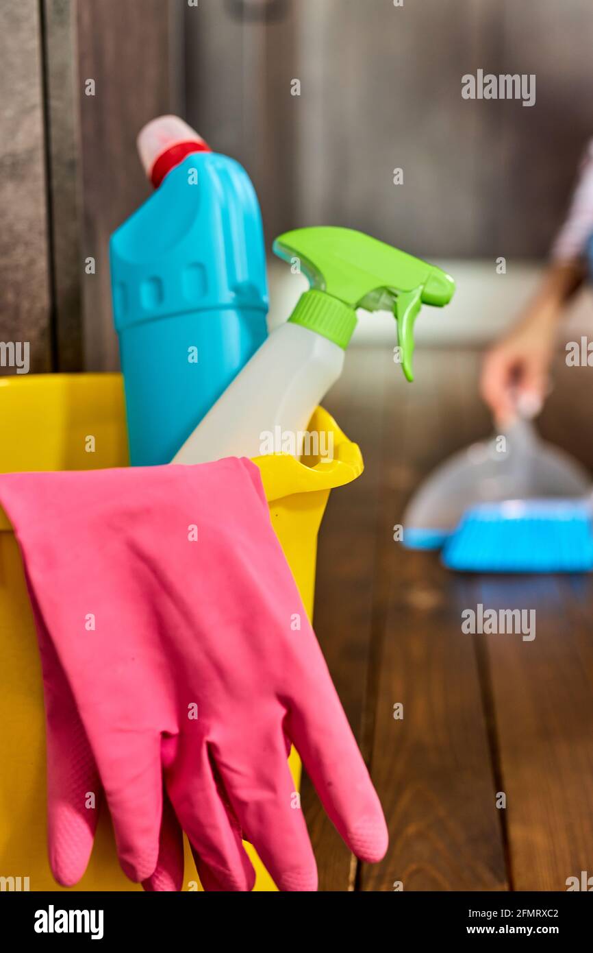 Konzentrieren Sie sich auf Eimer mit Gummihandschuhen und Waschmitteln im Inneren, weibliche Hausfrau entfernen Staub und Schmutz vom Boden mit Bürste und Kehrschaufel, Reinigung h Stockfoto