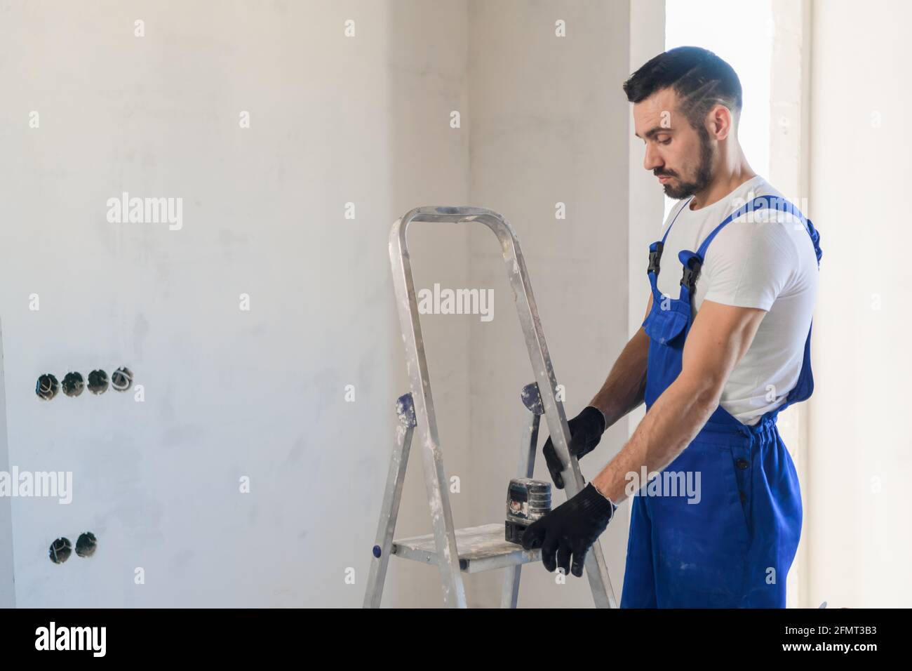 Ein Baumeister in Uniform verwendet ein elektronisches Lineal zum Markieren Die Wand Stockfoto