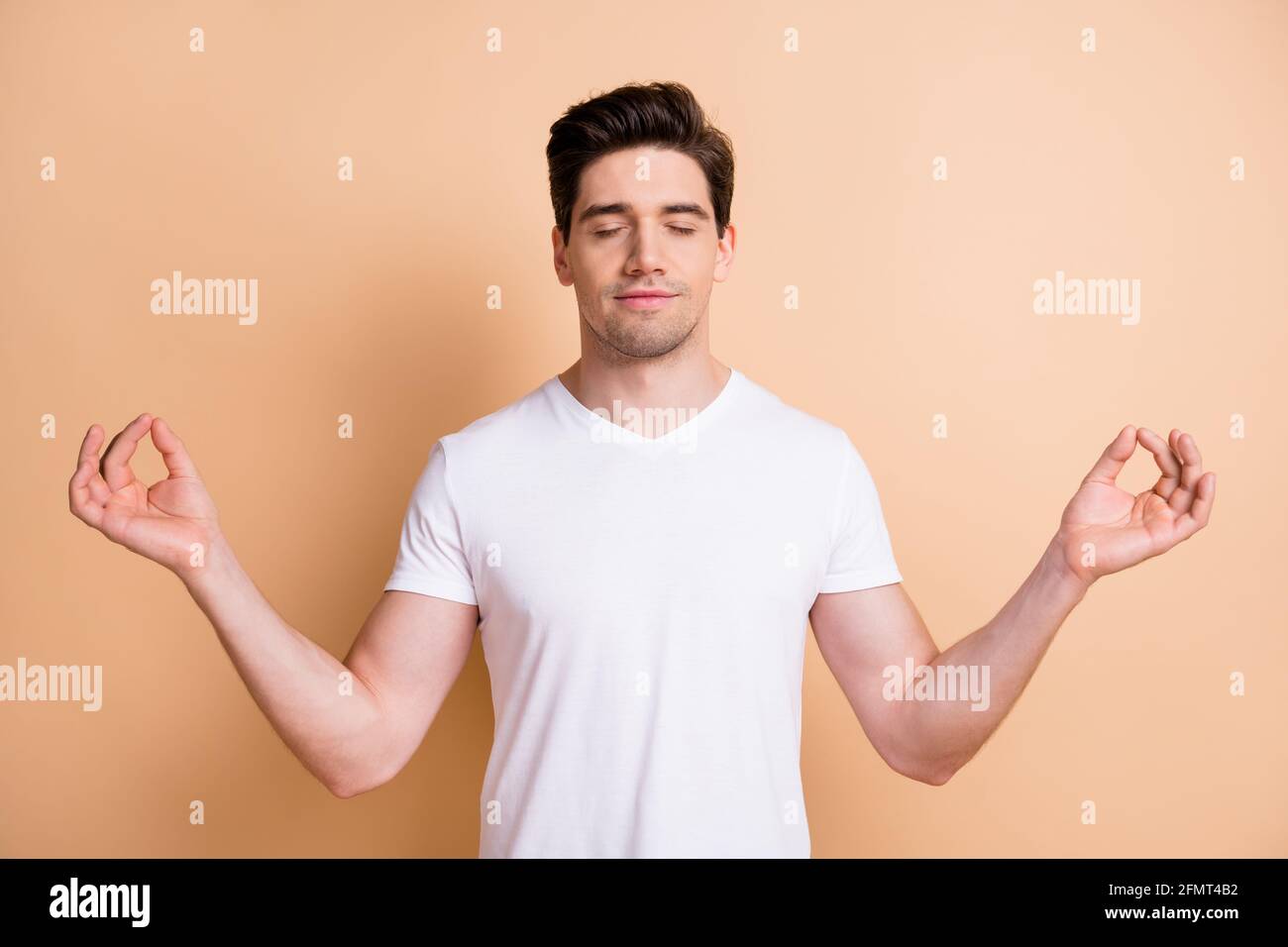 Porträt des optimistischen Brunet Mann gekreuzt Daumen tragen weißes T-Shirt Isoliert auf beigefarbenem Hintergrund Stockfoto